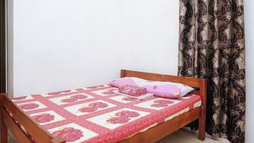 A single bed with a floral bedspread, a wooden headboard, and a curtain with a paisley pattern.