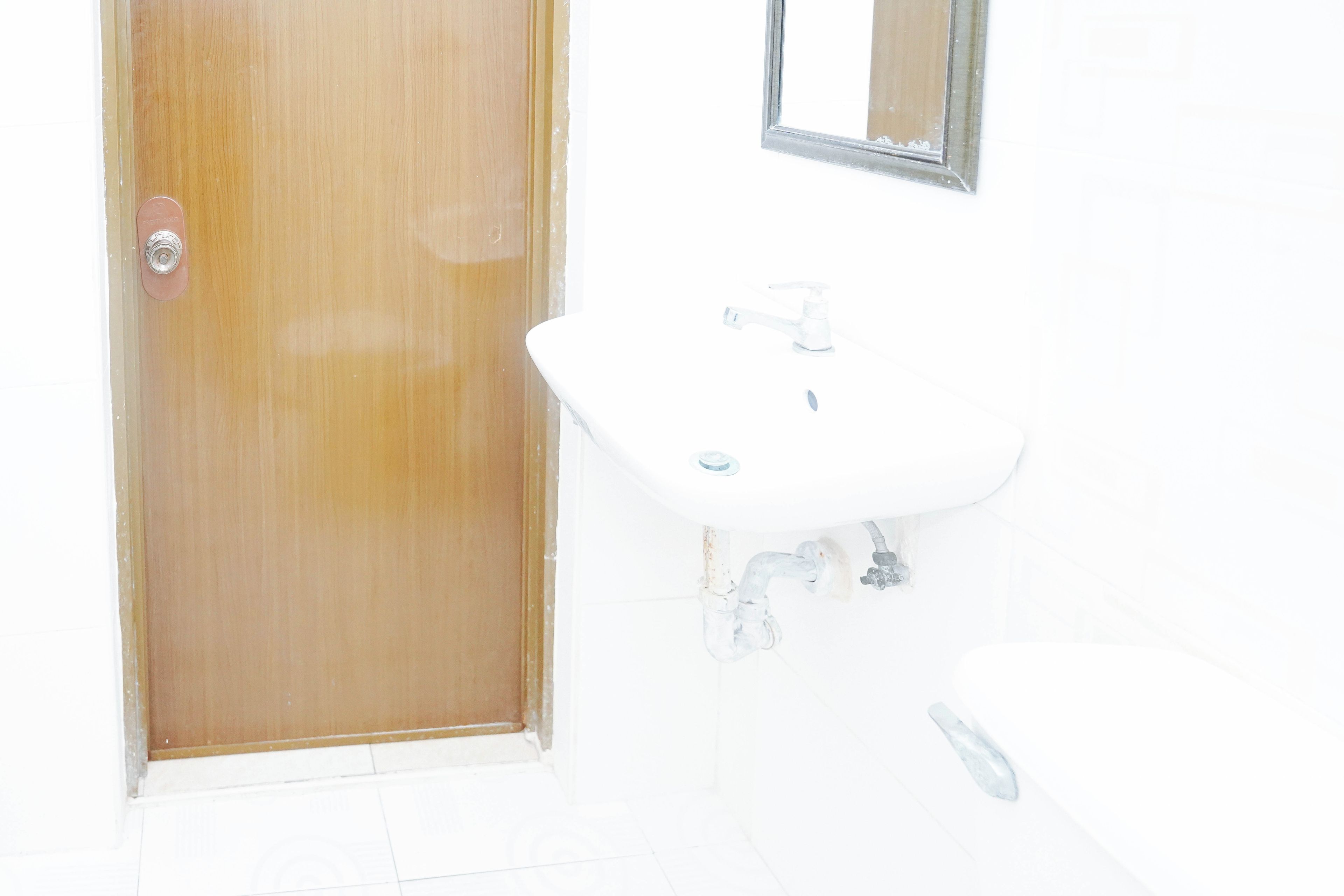 Ein Badezimmer mit Holztür, Waschbecken in Weiß und einem Spiegel an der Wand.