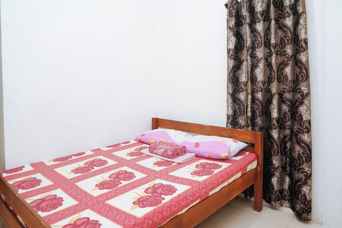 A single bed with a floral-patterned bedspread, a wooden headboard, and a curtain with a paisley design.