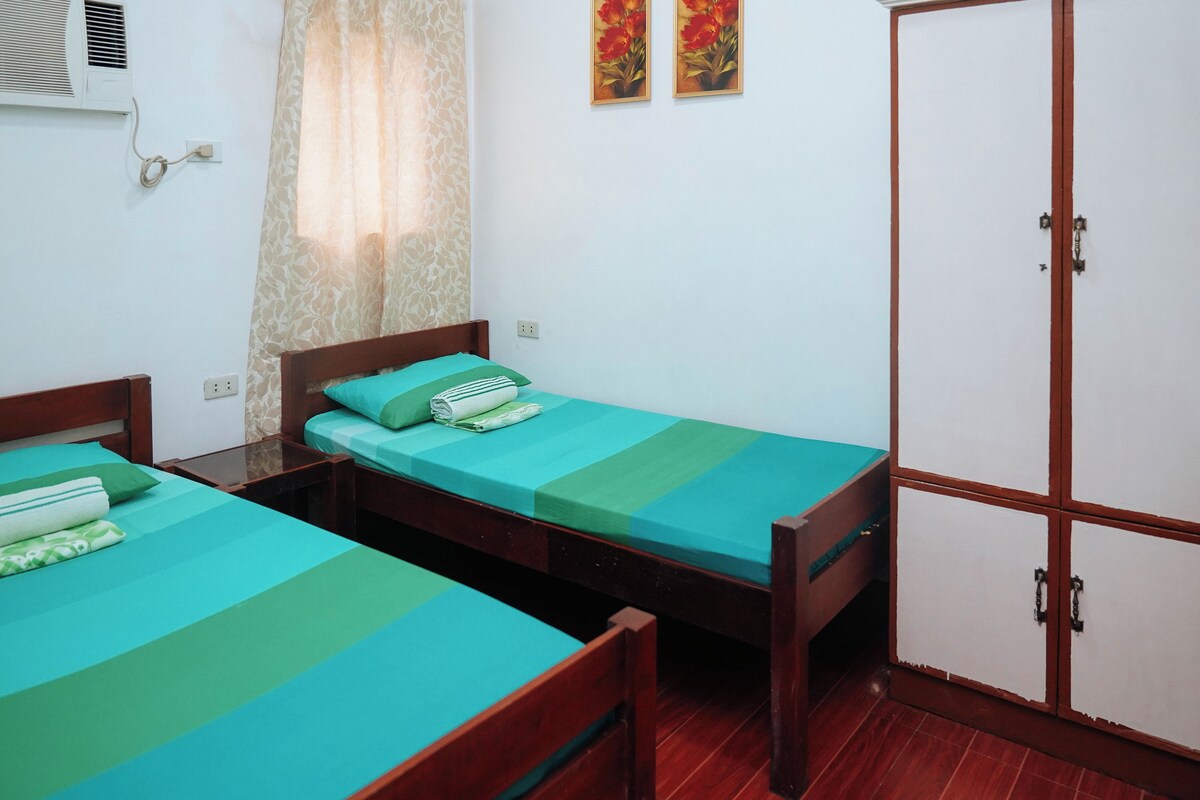 A room with two single beds, a wardrobe, and a window with curtains.