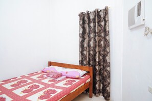 A single bed with a floral-patterned bedspread and a wooden headboard. A window with a white air conditioning unit is visible to the right. - C Star Travellers Inn Redpartner (Oslob)