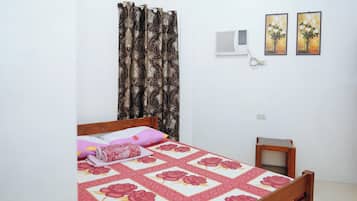A bedroom with a bed, a small bedside table, a wall-mounted air conditioner, and two framed pictures on the wall.