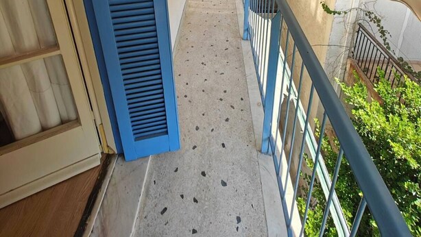 Un couloir étroit avec des volets bleus, un sol en béton et une rambarde en métal.
