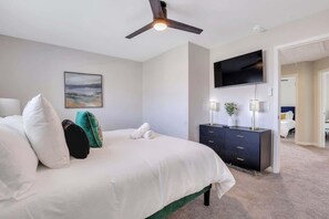 Un dormitorio con cama, ventilador de techo, televisión, cómoda y un cuadro en la pared.