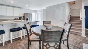Une cuisine moderne avec des meubles blancs, un plan de travail en granit et un coin repas comprenant une table ronde et des chaises.