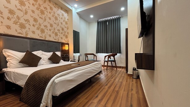 A hotel room with a large bed, a desk, a chair, a TV, and a patterned wall. - Hotel Down Town (Jaipur)