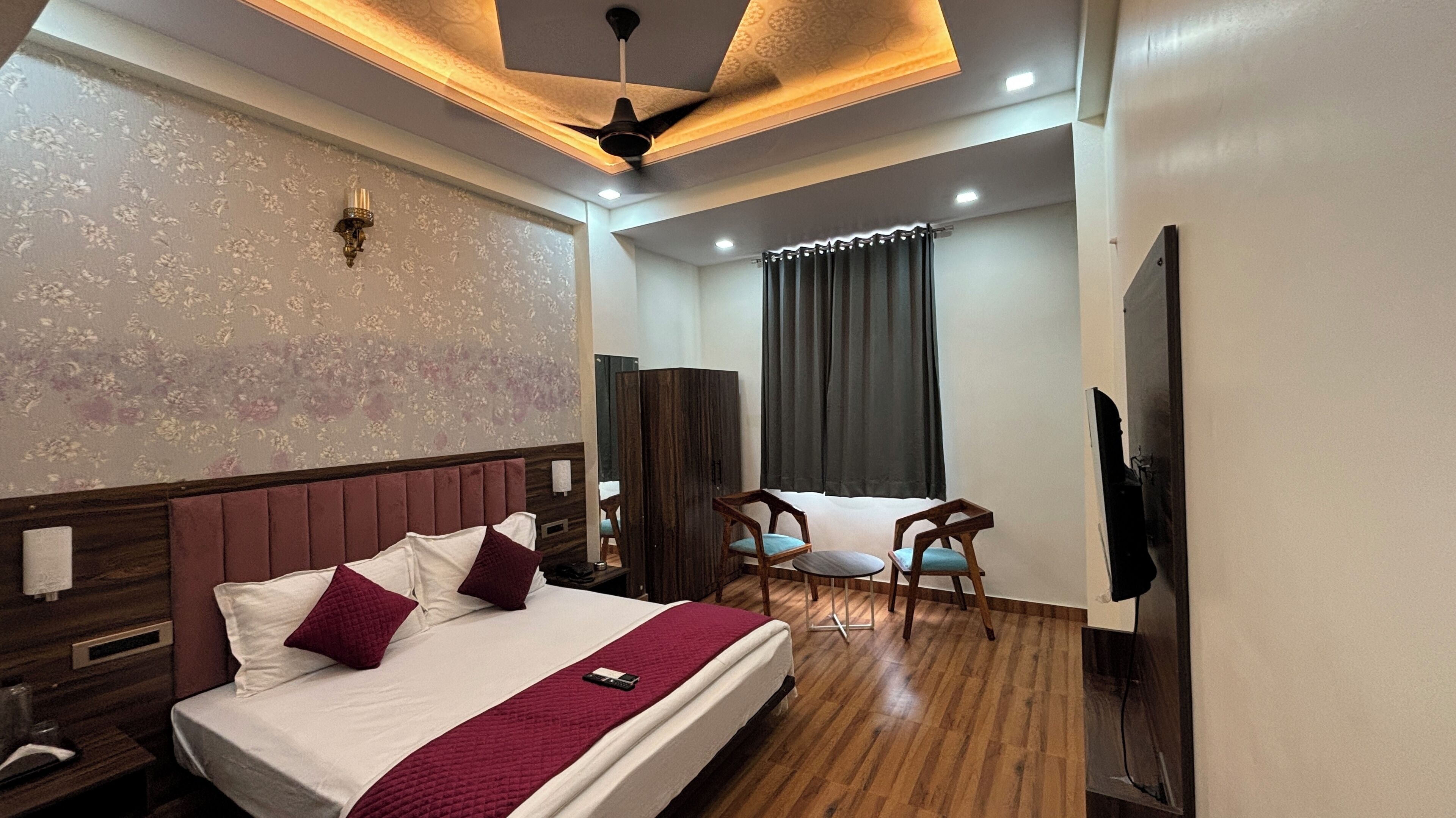 A hotel room with a bed, a wooden headboard, a ceiling fan, a TV, a desk, and a chair.