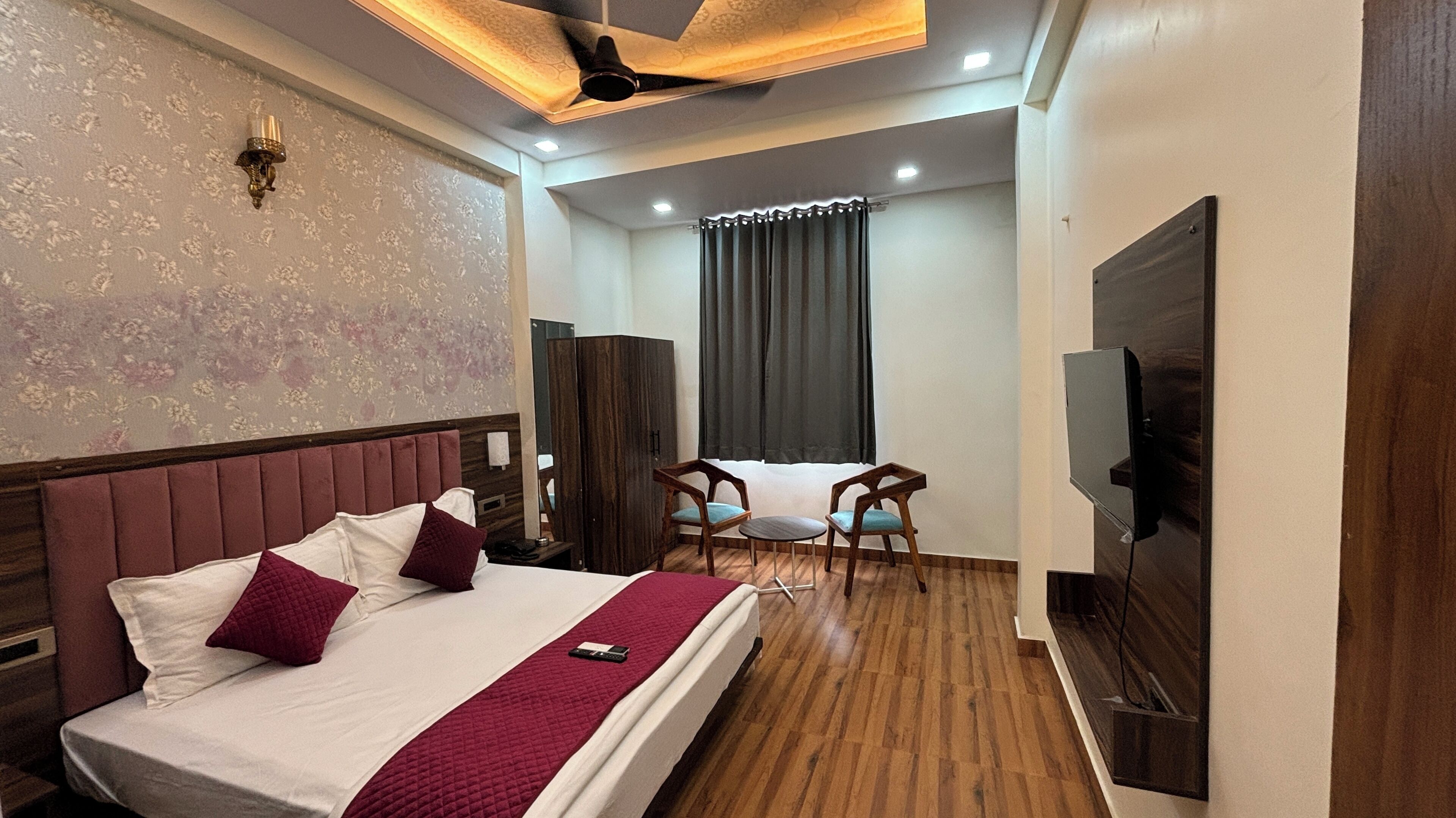 A hotel room with a large bed, a TV, a ceiling fan, and a seating area with chairs and a table.