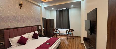 A hotel room with a large bed, a TV, a ceiling fan, and a seating area with chairs and a table.