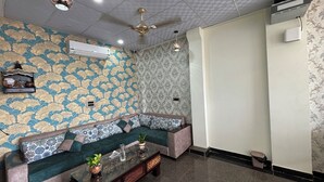 A room with a patterned wall, a sofa with cushions, a glass coffee table, and a ceiling fan. - Hotel Down Town (Jaipur)