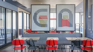 A modern cafeteria with red and black chairs, white tables, and abstract wall art.