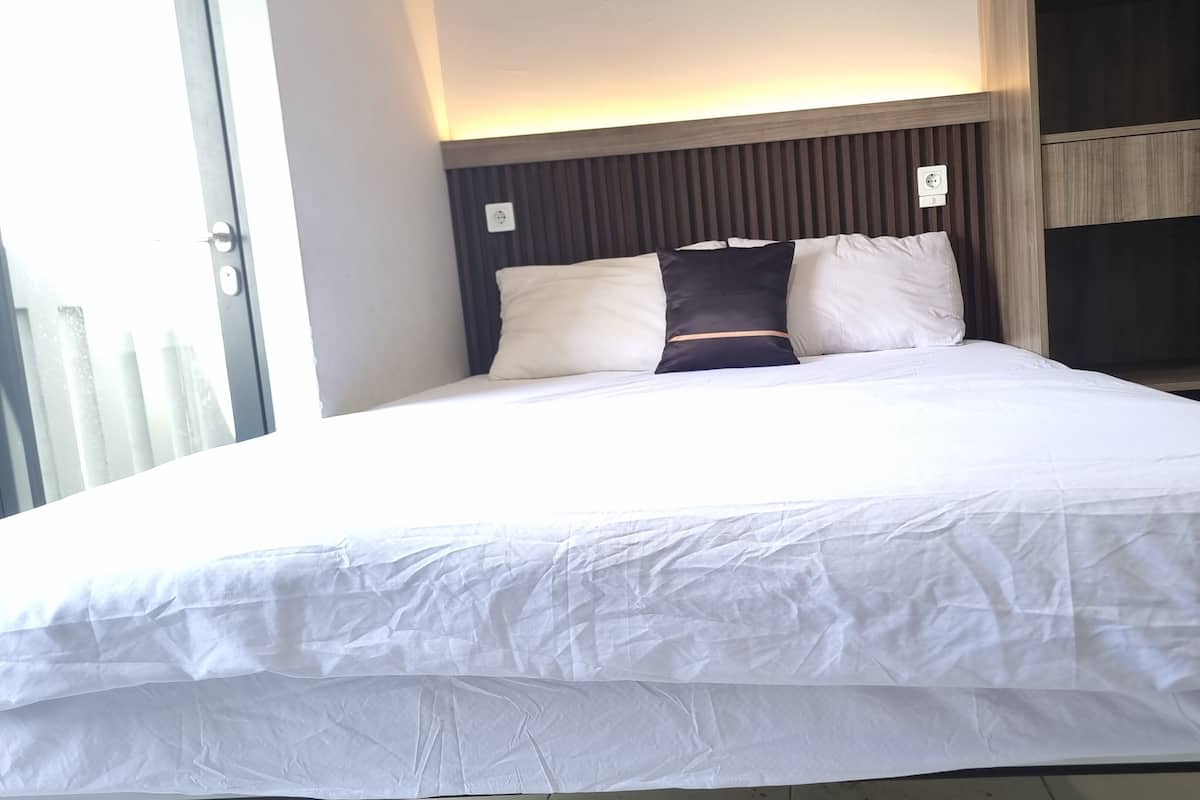 A neatly made bed with white bedding and two pillows, a wooden headboard, and a power outlet on the wall.