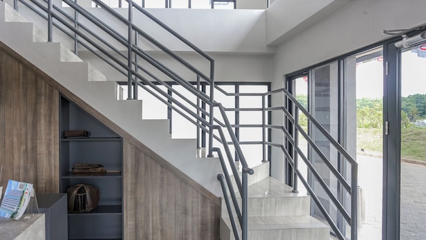 A modern staircase with metal railings, a wooden shelf unit, and a view of the outdoors.
