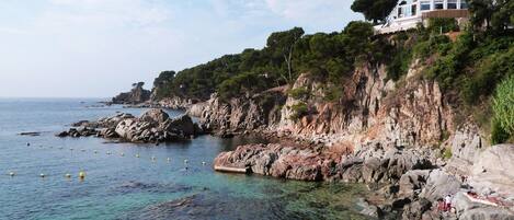 A coastal property with rocky cliffs, clear water, and a building with balconies overlooking the sea.