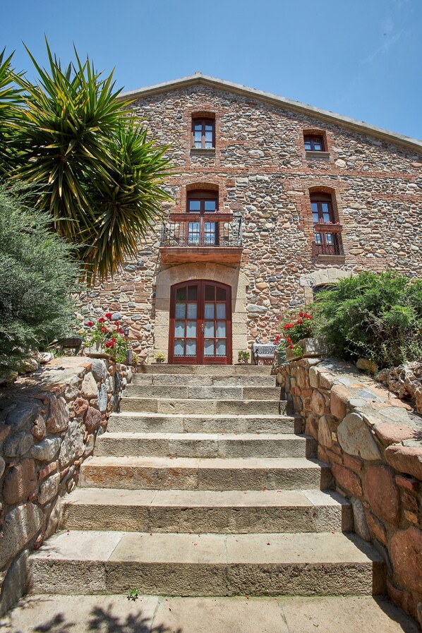 A stone building with a central entrance, steps leading up to it, and a balcony with railings.