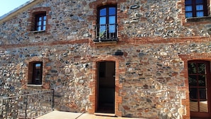 A stone building with a tiled patio, a balcony, and a door leading to an interior space. - Rincón de Piedra a 30' de Barcelona (Corró d'Avall)