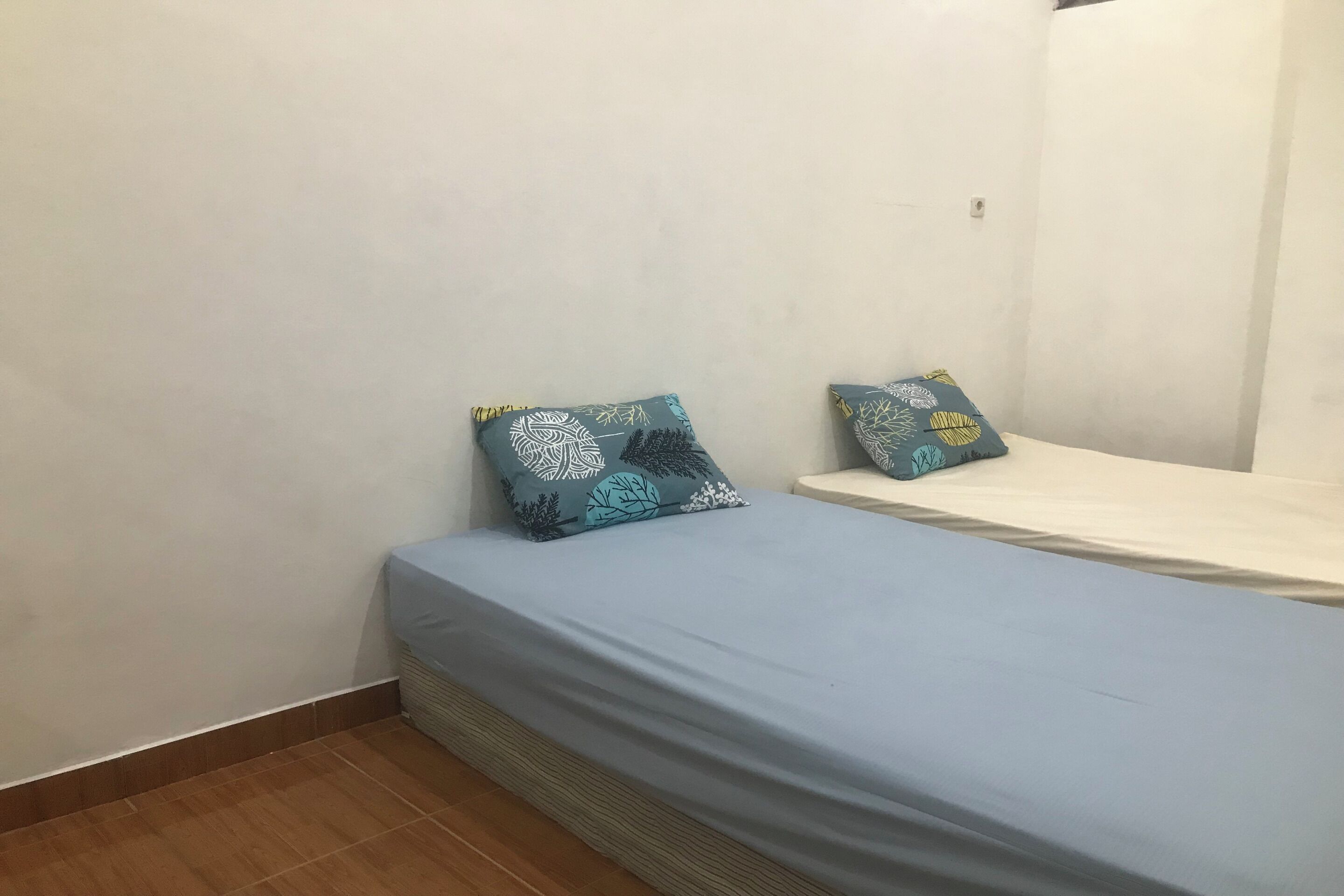 A small, simple room with a single bed, two pillows, and a plain wall.