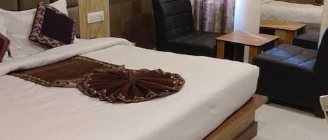 A hotel room with a large bed, a headboard, an air conditioning unit, a chair, a small table, and a mirror.