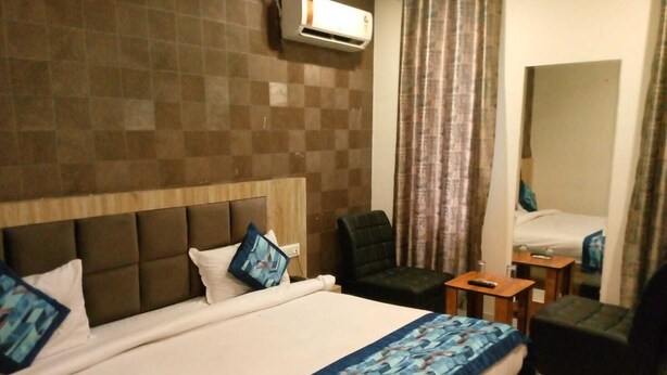 A hotel room with a large bed, a chair, a small table, and a mirror. - Hotel Glass INN (Dera Bassi)