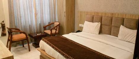 Una habitación de hotel con una cama grande, un cabecero de madera, una mesita de noche, una silla y una cortina.