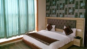 A bedroom with a large bed, a wooden headboard, and a window with sheer curtains. - Hotel Glass INN (Dera Bassi)