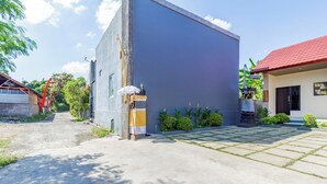 A modern building with a grey facade, a red-roofed adjacent structure, and a paved courtyard with greenery. - OYO 94152 Pondok Wisata Alan Dinah (Seririt)