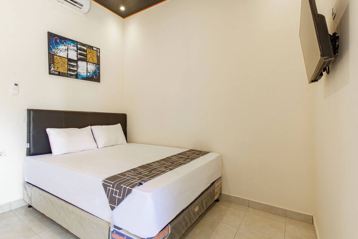 A neatly made bed with a white and brown bedspread, a headboard, and a wall-mounted TV.