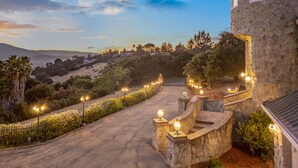 A stone building with a curved roof, surrounded by a landscaped garden with a winding path and street lamps. - Grand Villa Castle in San Jose (San Jose)
