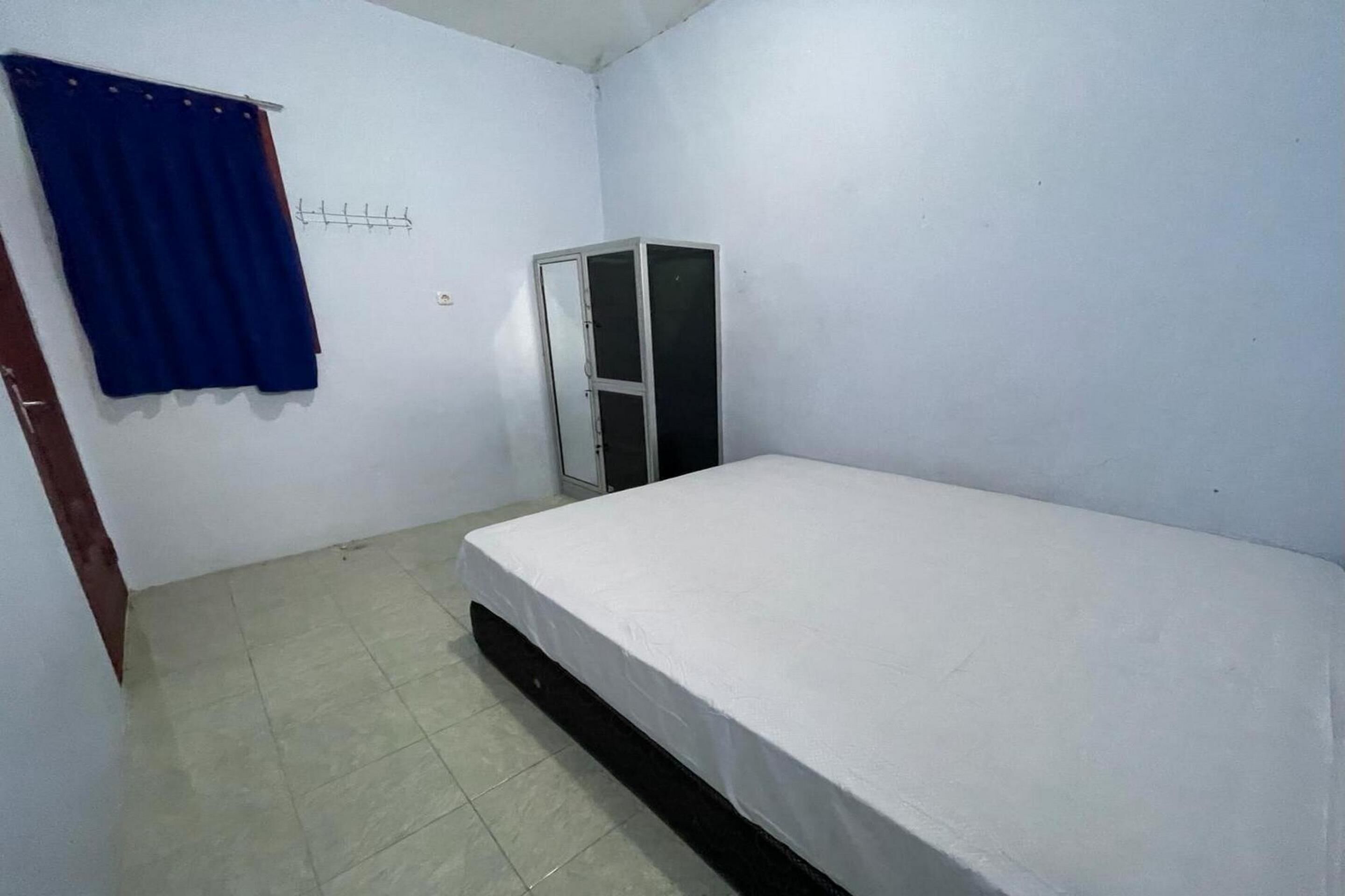 Een kleine, schone kamer met een enkel bed, een kledingkast en een blauw gordijn.