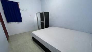 Een kleine, schone kamer met een enkel bed, een kledingkast en een blauw gordijn.