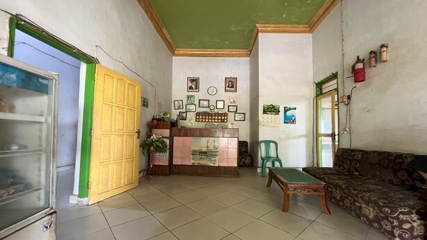 A reception area with a tiled floor, a reception desk, a green chair, a sofa, and a refrigerator. - Hotel O Kost Btnompo Near SDI Bontosallang (Bontonompo)