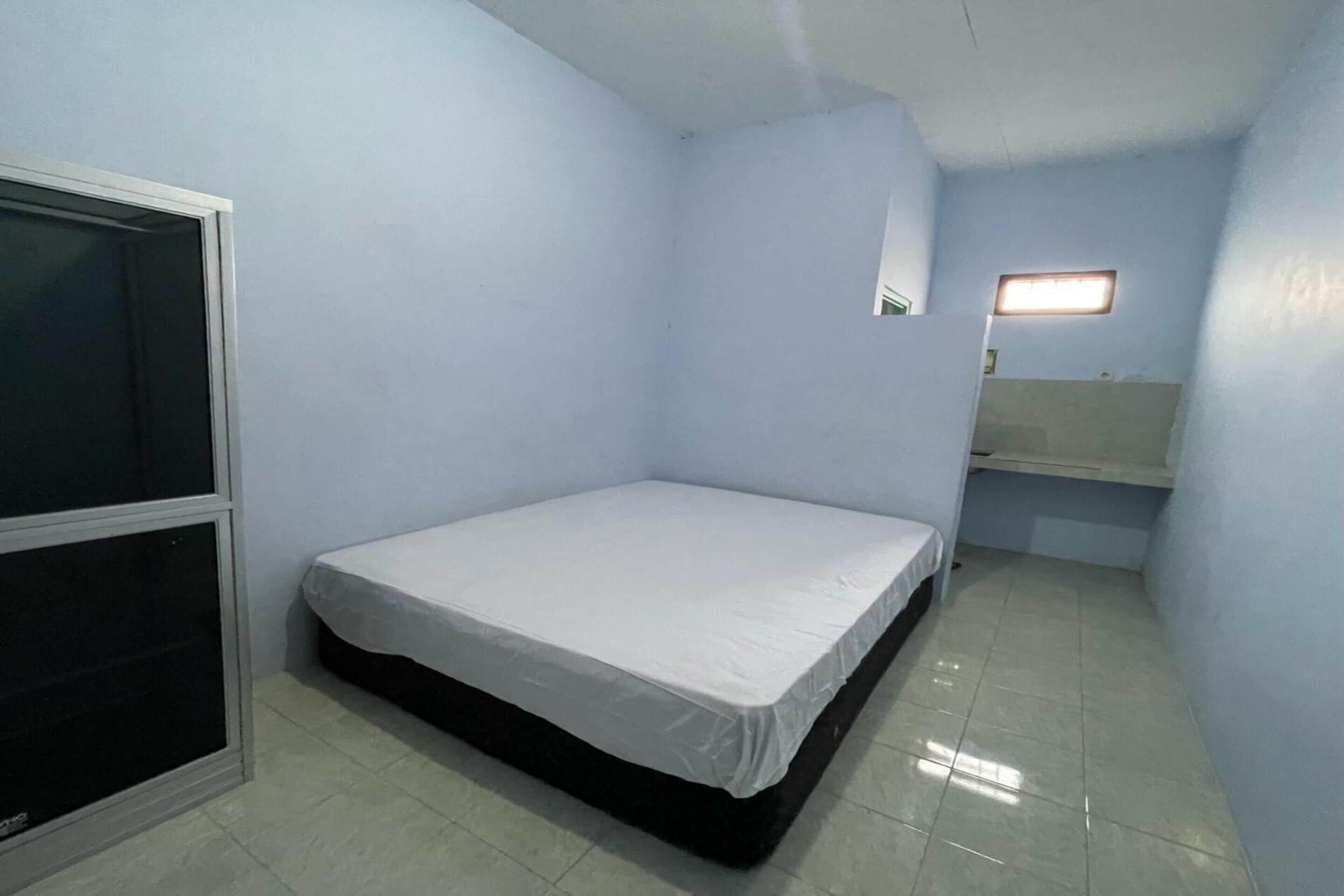Una habitación pequeña con cama individual, ventana, espejo y lámpara.