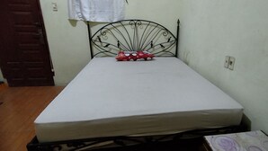Une petite chambre avec un lit simple, dotée d’une tête de lit en métal, d’un matelas blanc et d’un oreiller rouge à pois blancs.