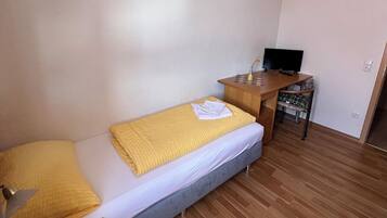 Una habitación pequeña y ordenada con cama, escritorio y televisión.