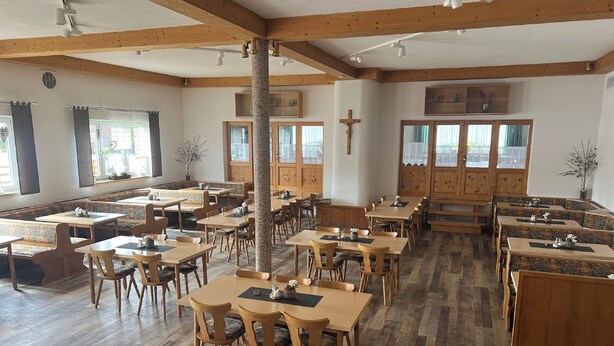 Un vaste espace dédié à la salle à manger, avec des tables et des bancs en bois, de grandes fenêtres et une croix accrochée au mur.