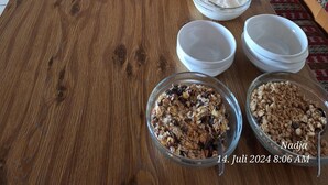 Un buffet de petit-déjeuner comprenant une table en bois, différentes sortes de pain, une planche de charcuterie, ainsi que des bols de yaourt et de granola.