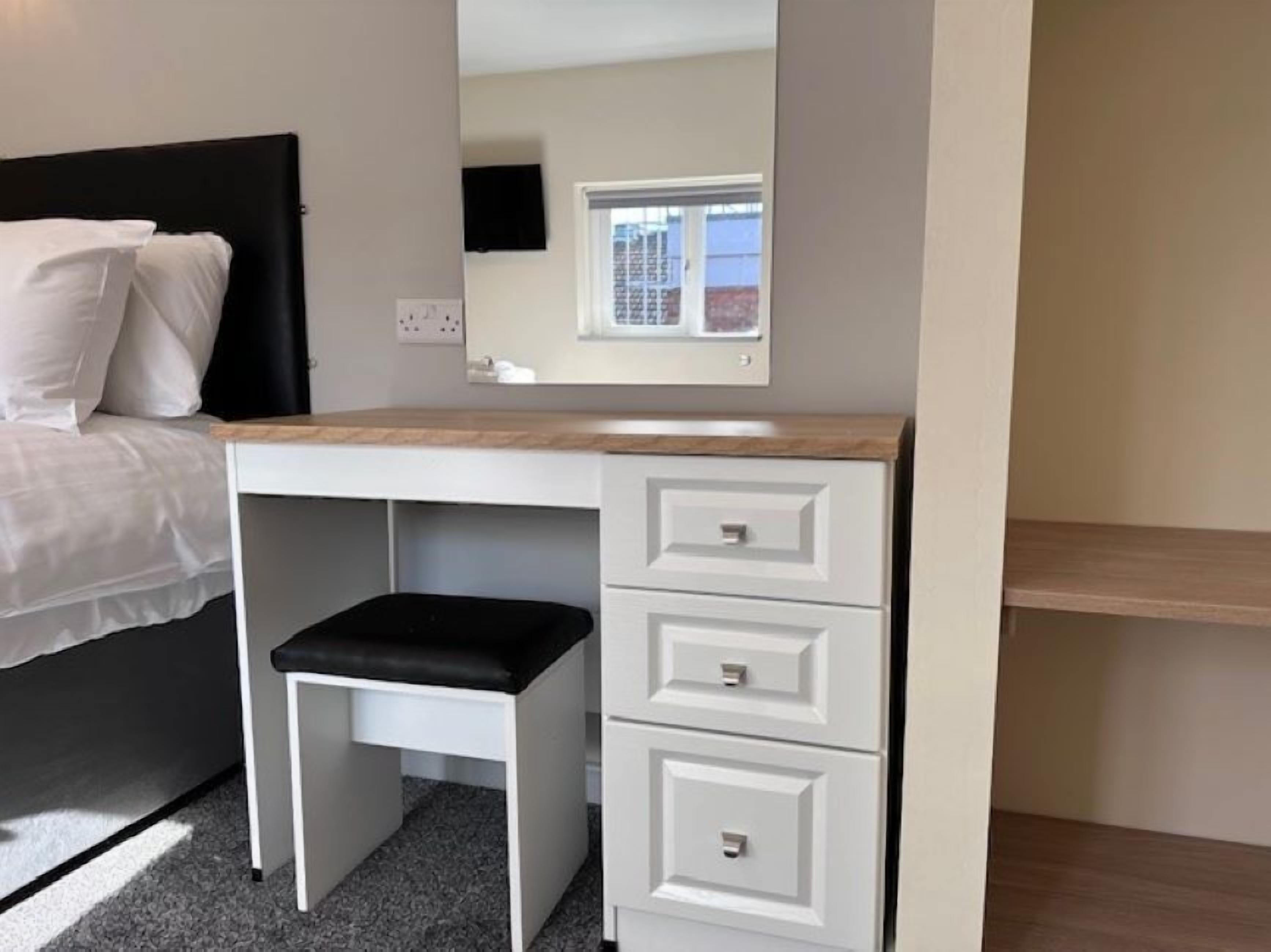A bedroom with a bed, a white dresser with drawers, a mirror, and a window.