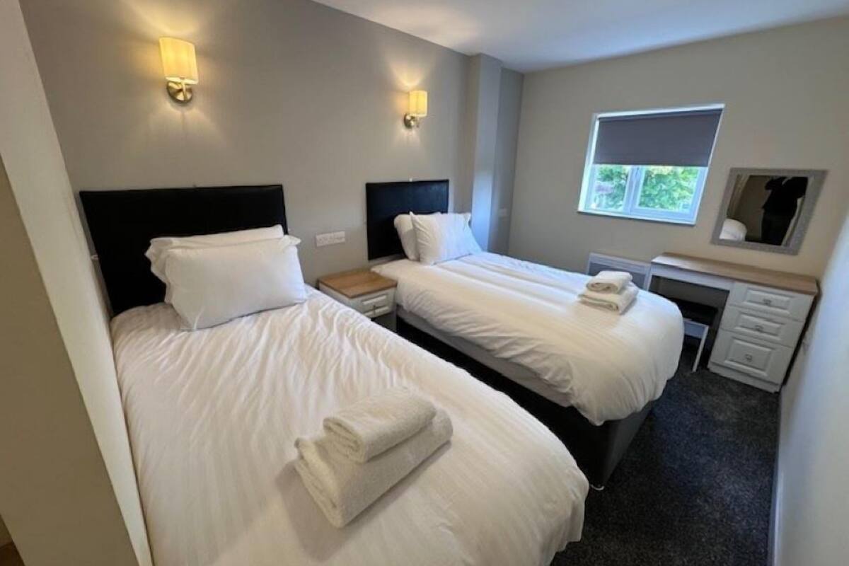 A hotel room with two beds, a desk, a mirror, and two wall-mounted lights.
