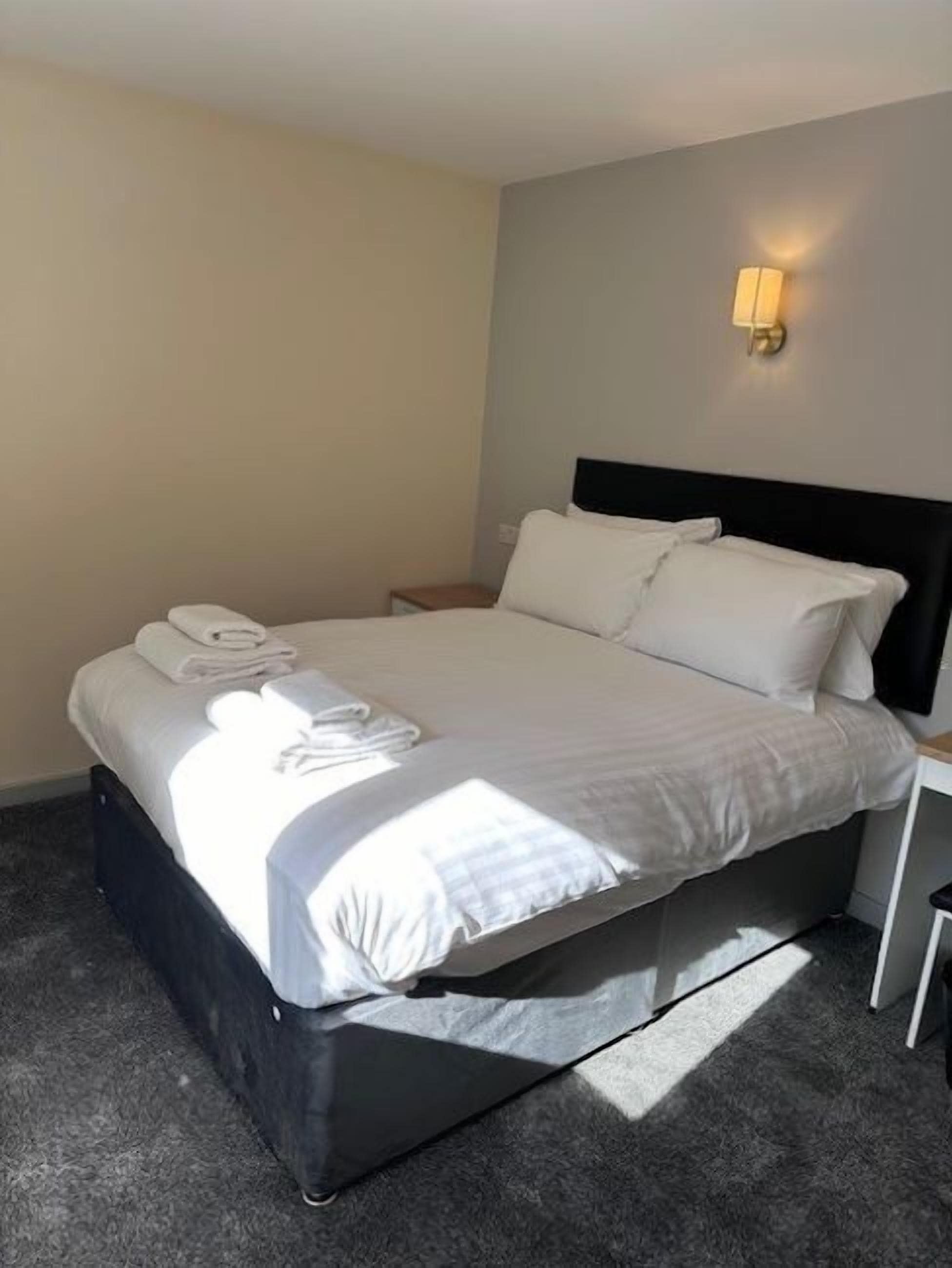 A neatly made bed with white linens and towels, a black headboard, and a bedside table with a lamp.