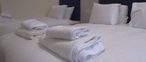 A hotel room with two beds, each with neatly folded white towels and matching pillows.