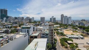 A cityscape with high-rise buildings, a parking area with buses, and a clear sky. - Lotus Rock Hotel DN by Bay Luxury (Da Nang)