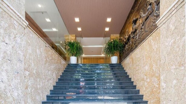 A marble staircase with two potted plants on the sides, leading to a wooden door at the top. - Lotus Rock Hotel DN by Bay Luxury (Da Nang)