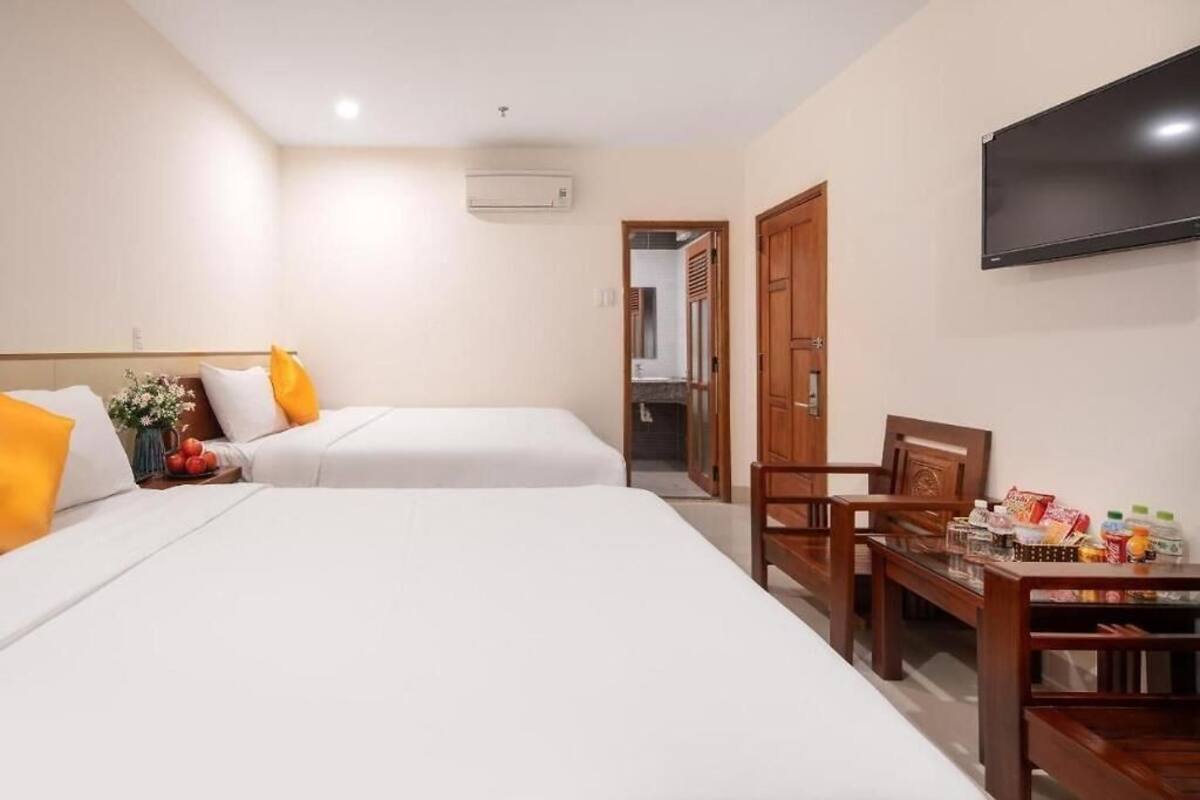 Quarto de hotel com duas camas, televisão, mesa de madeira com lanches e porta para um banheiro.