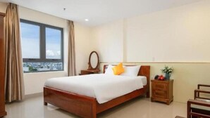 A hotel room with a large bed, a nightstand, a mirror, and a view of a cityscape through the window. - Lotus Rock Hotel DN by Bay Luxury (Da Nang)