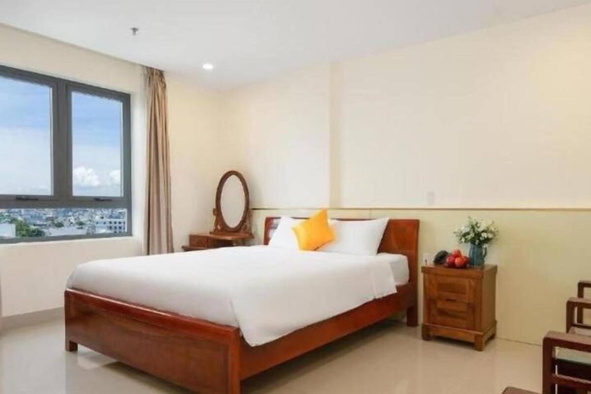 Quarto de hotel com uma cama grande, uma mesa de cabeceira, um espelho e vista para a cidade pela janela.