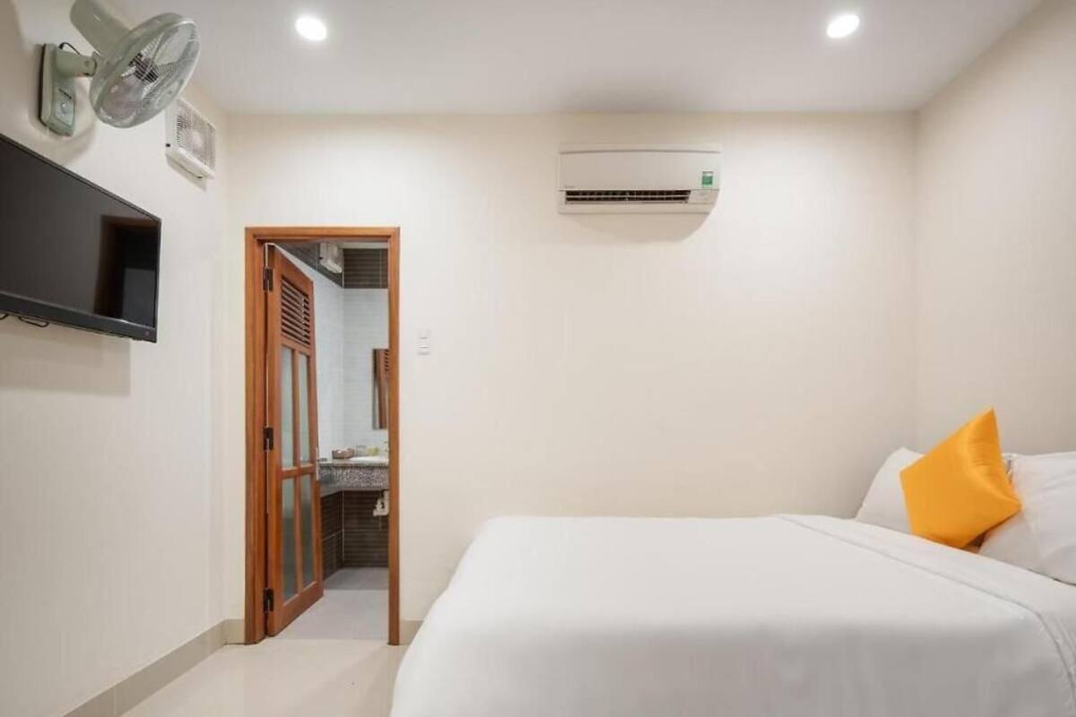 Quarto com cama, televisão, ar condicionado e banheiro visível por uma porta aberta.