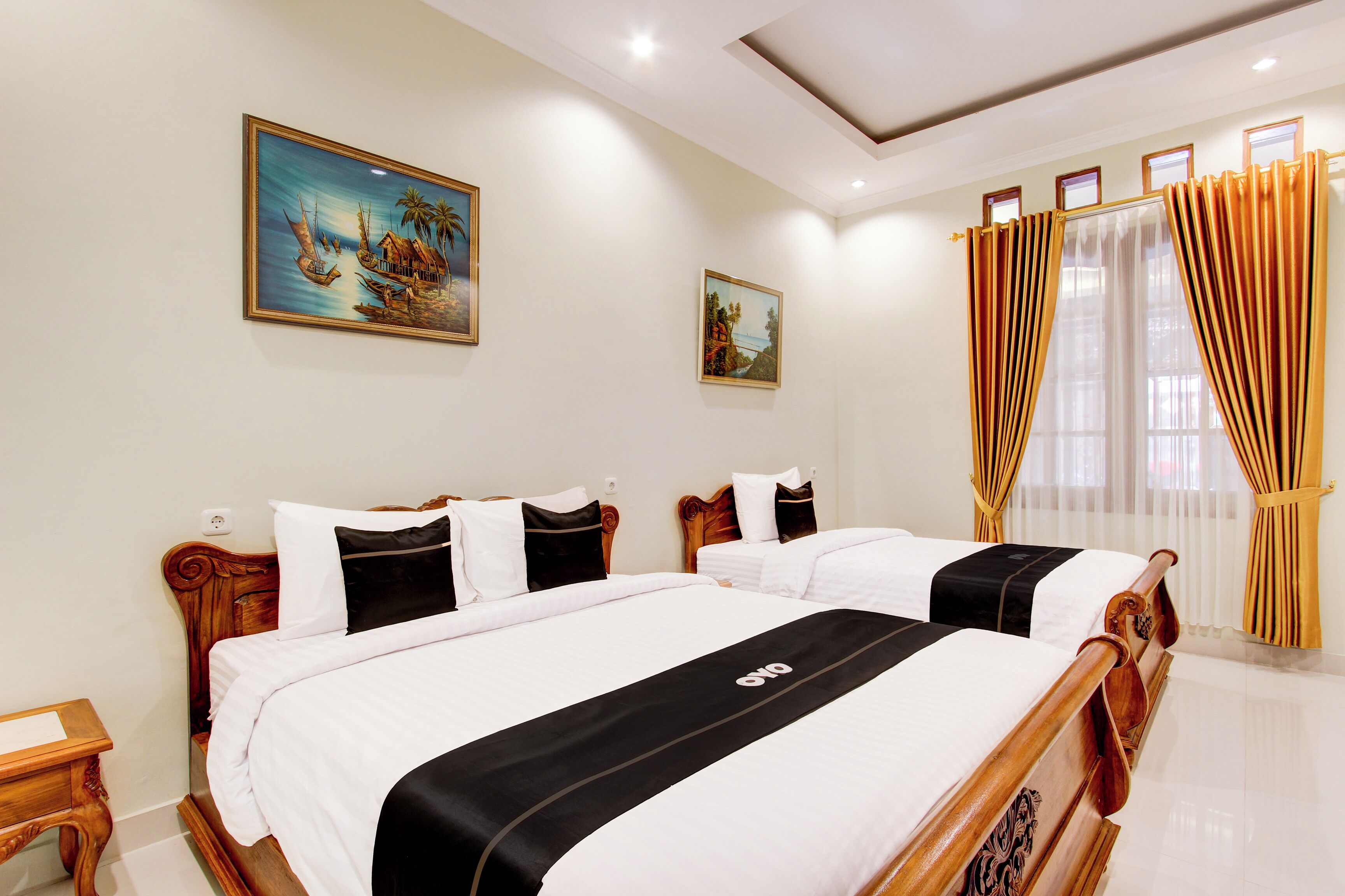 Une chambre d’hôtel avec deux lits, des têtes de lit en bois, du linge de lit blanc et un tableau représentant un paysage tropical.