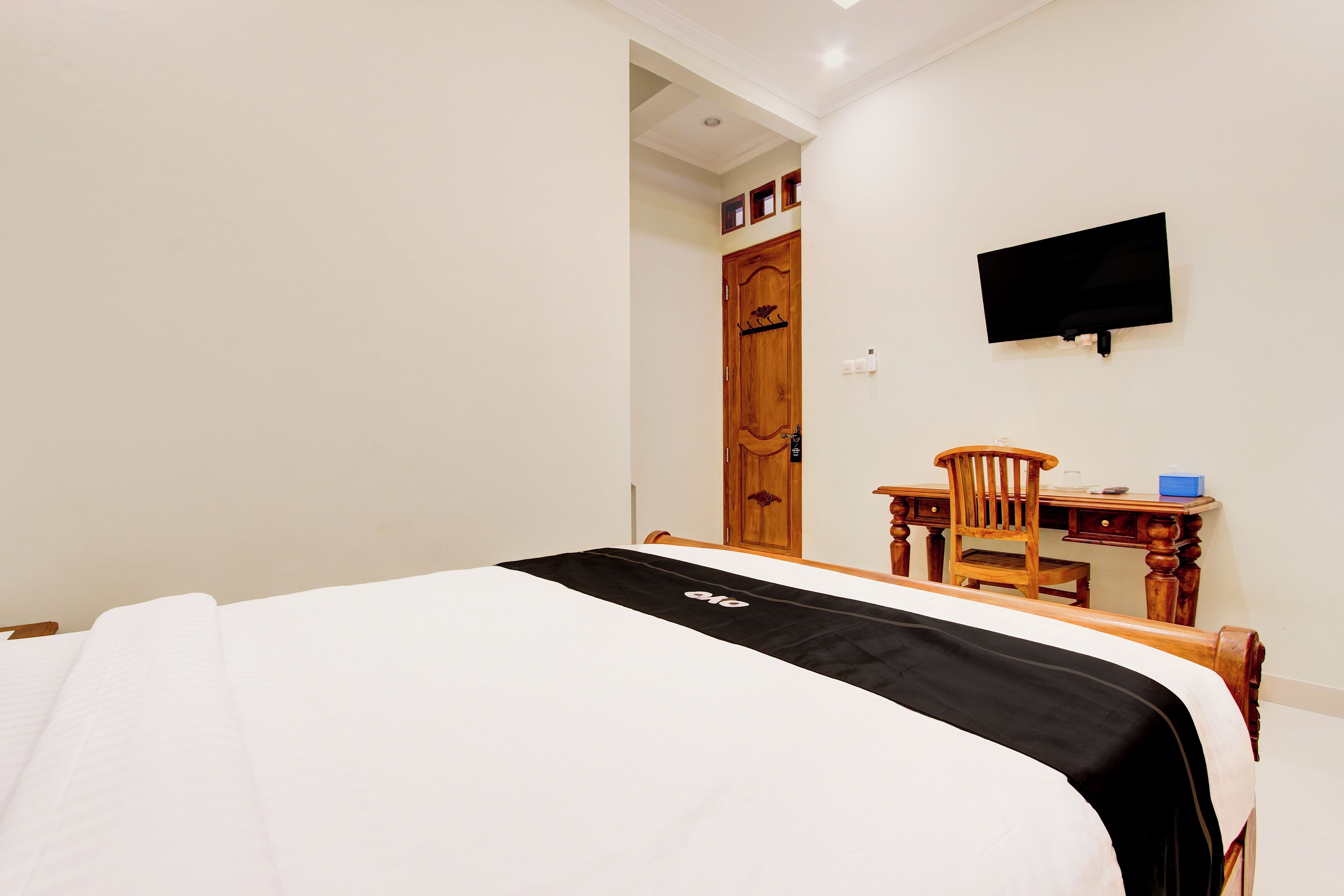 A bedroom with a bed, a desk, a chair, and a television on the wall.