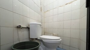 A small, tiled bathroom with a toilet, a trash bin, and a visible crack in the wall. - Hotel O Kost Aisyah Near Citra Grand Galesong City(Pattalassang) (Pattallassang)