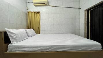 Una cama individual con ropa blanca en una habitación con paredes de baldosas y una ventana con cortina.